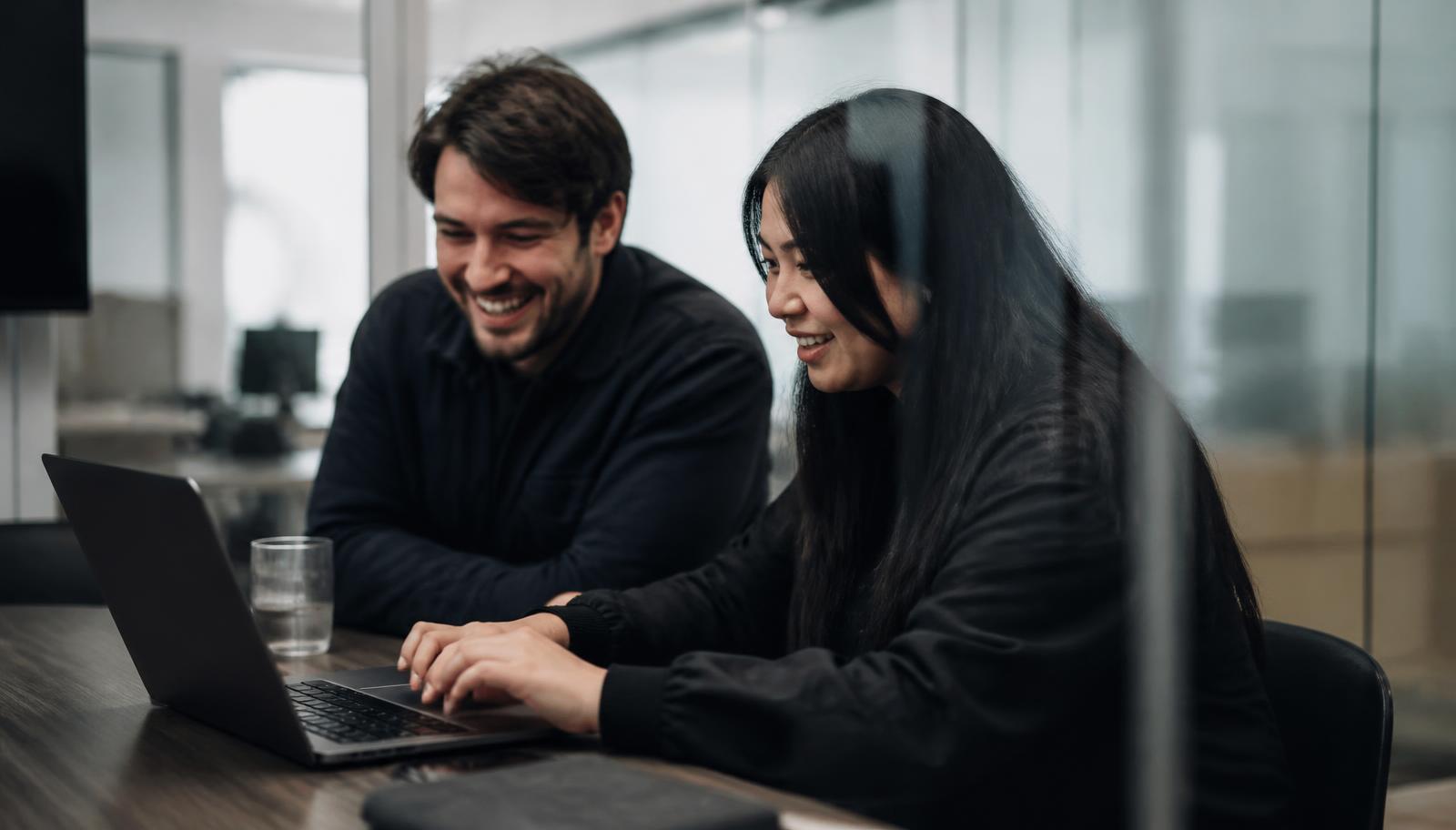 Two colleagues testing a customer chat assistant on a laptop in a glass meeting room