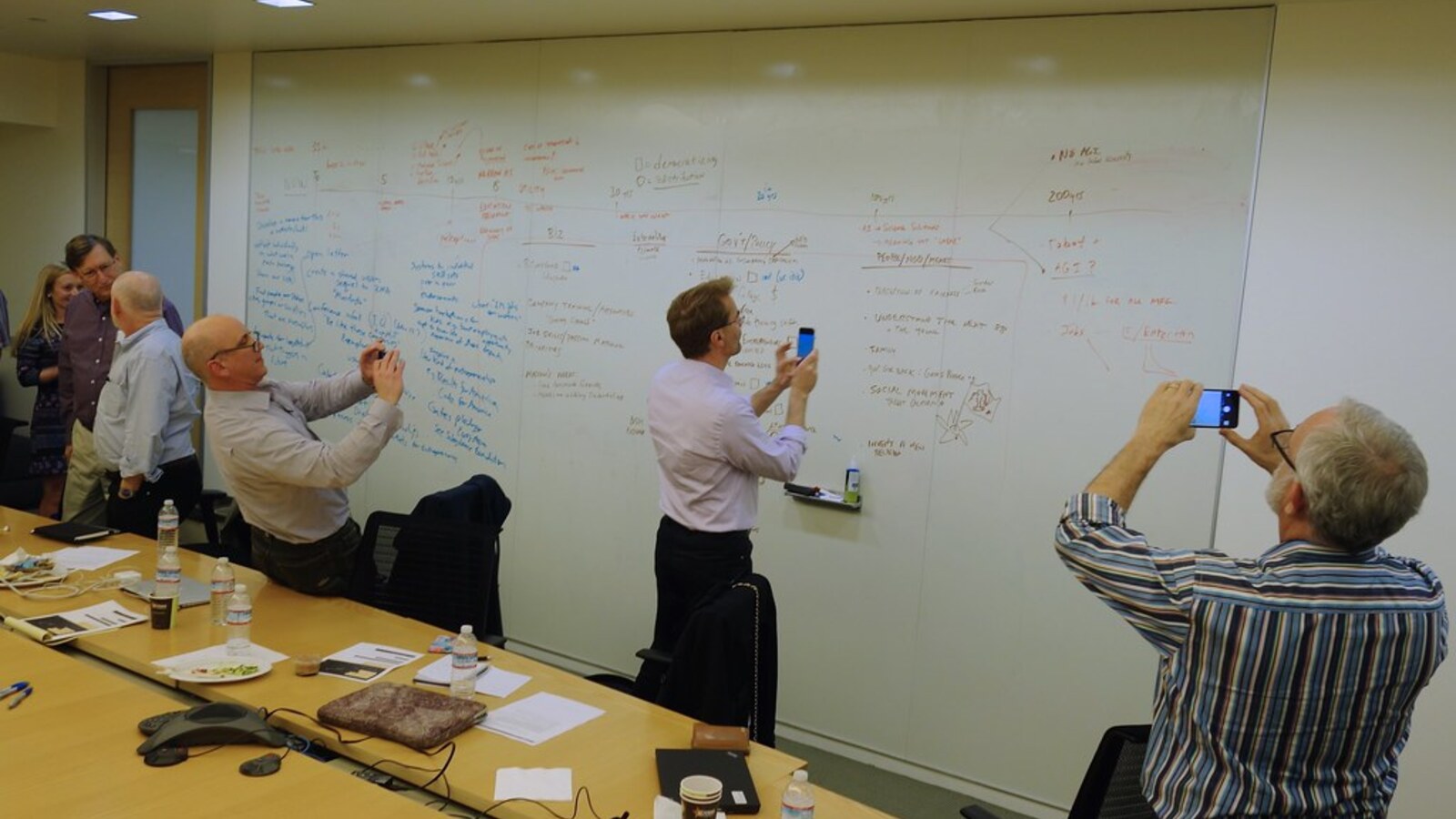 A small team at a whiteboard mapping competitor moves and pricing signals during a strategy session