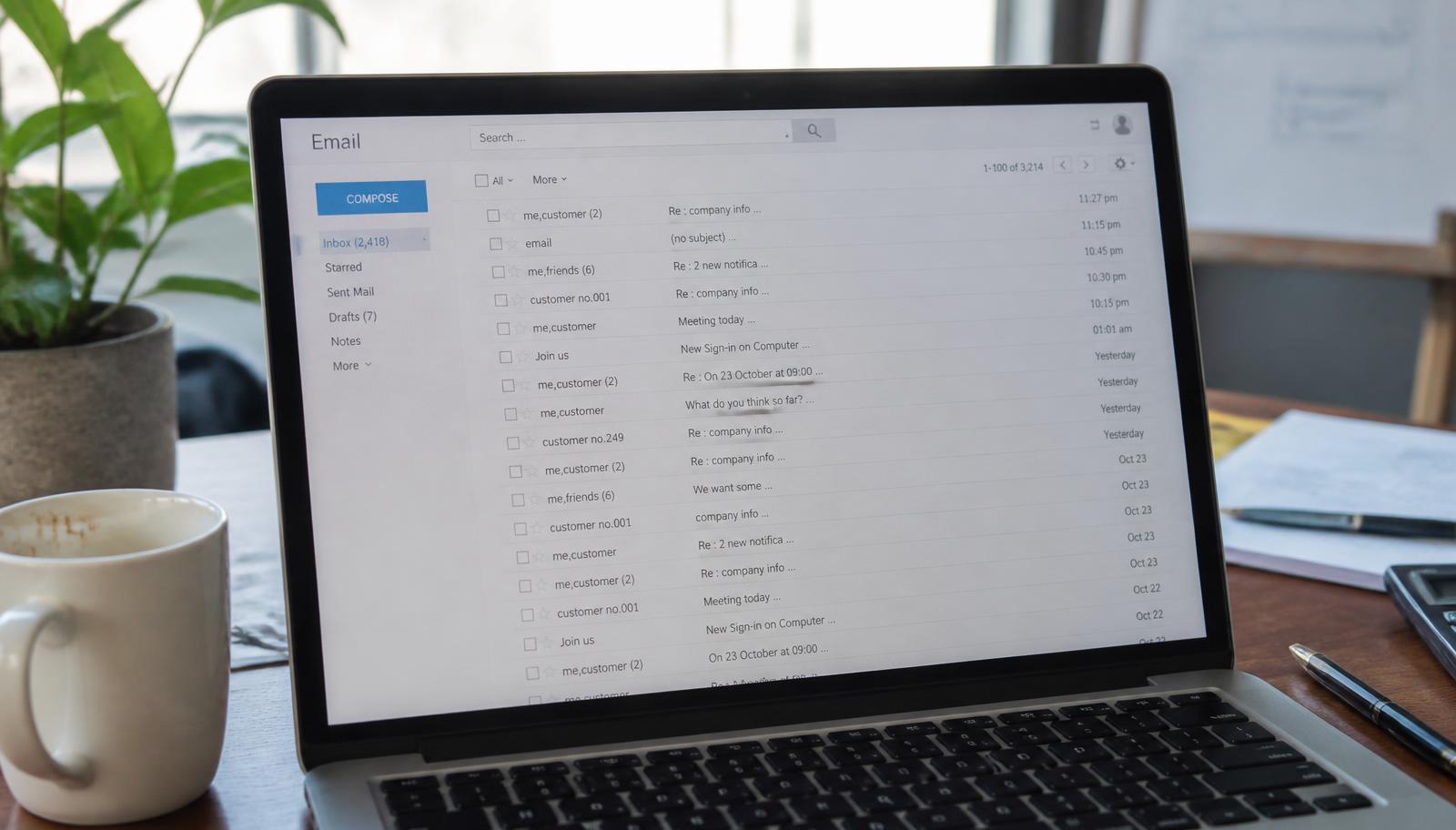 A laptop screen showing an email inbox with several unread threads, on a desk with a coffee cup
