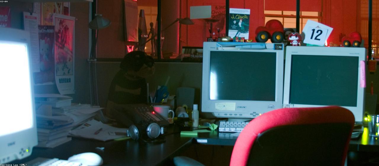 An office desk at dusk with a lamp on and a stack of processed documents beside a laptop