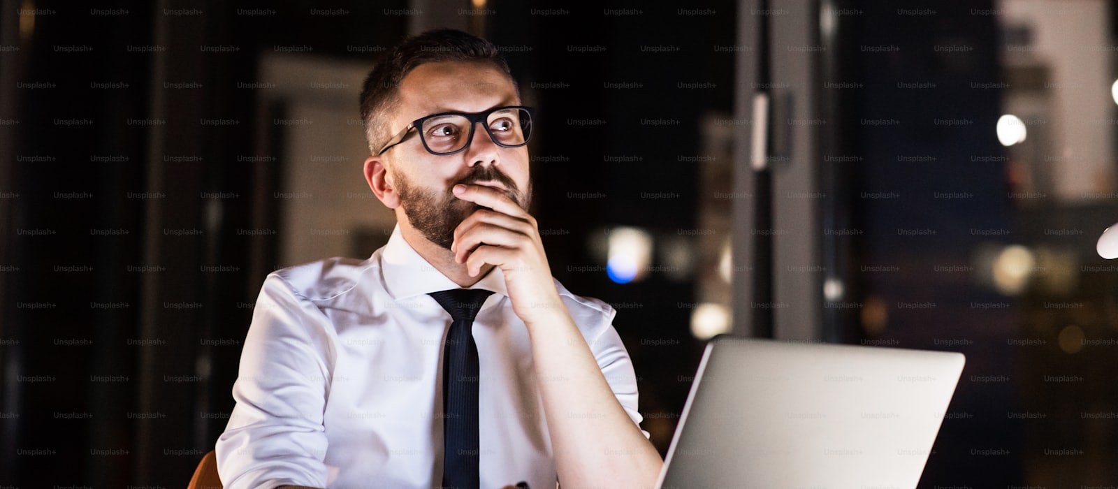 A marketer working late at a desk lit only by a laptop screen at dusk