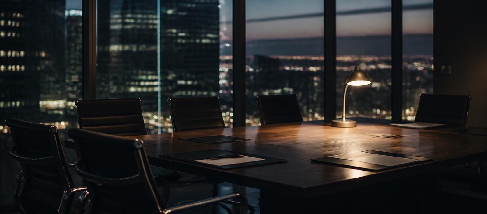 A corporate boardroom at dusk with folders on the table and one lamp lit