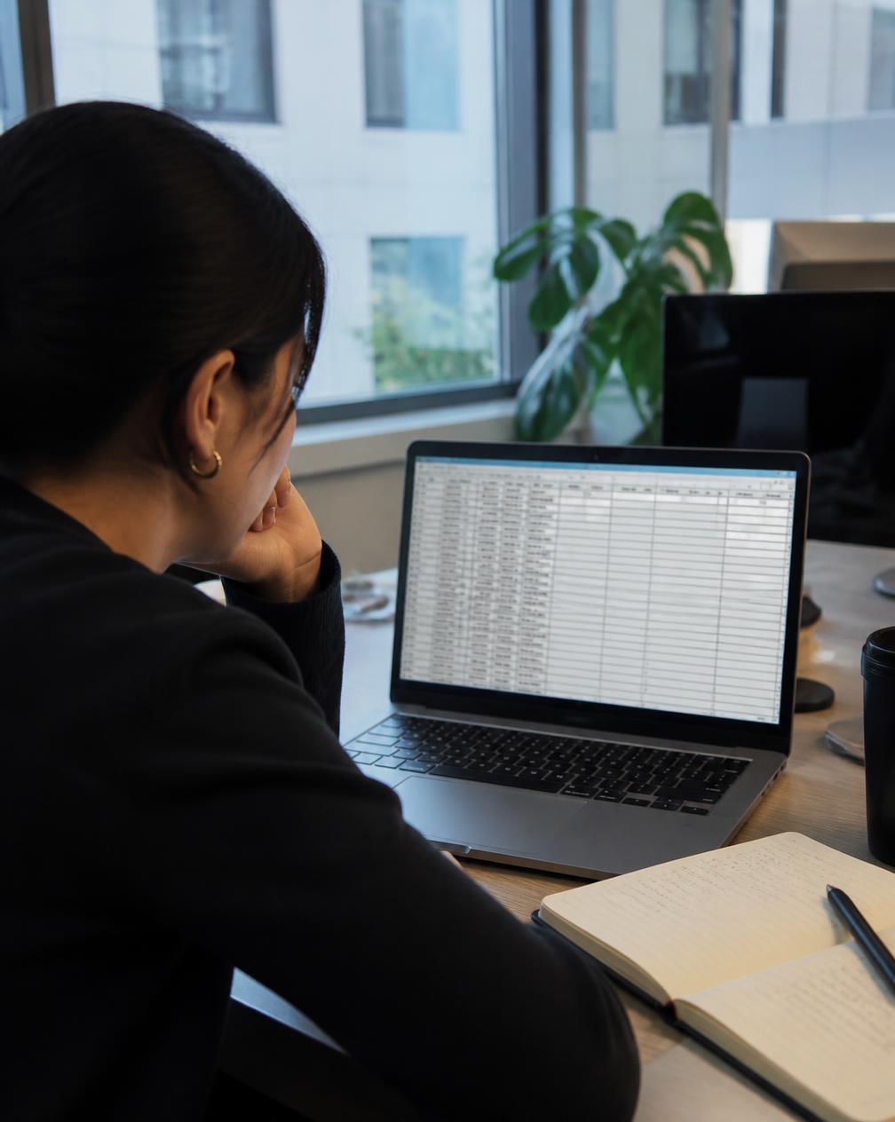 A data analyst at a laptop scrolling through a spreadsheet of lead records with missing fields highlighted