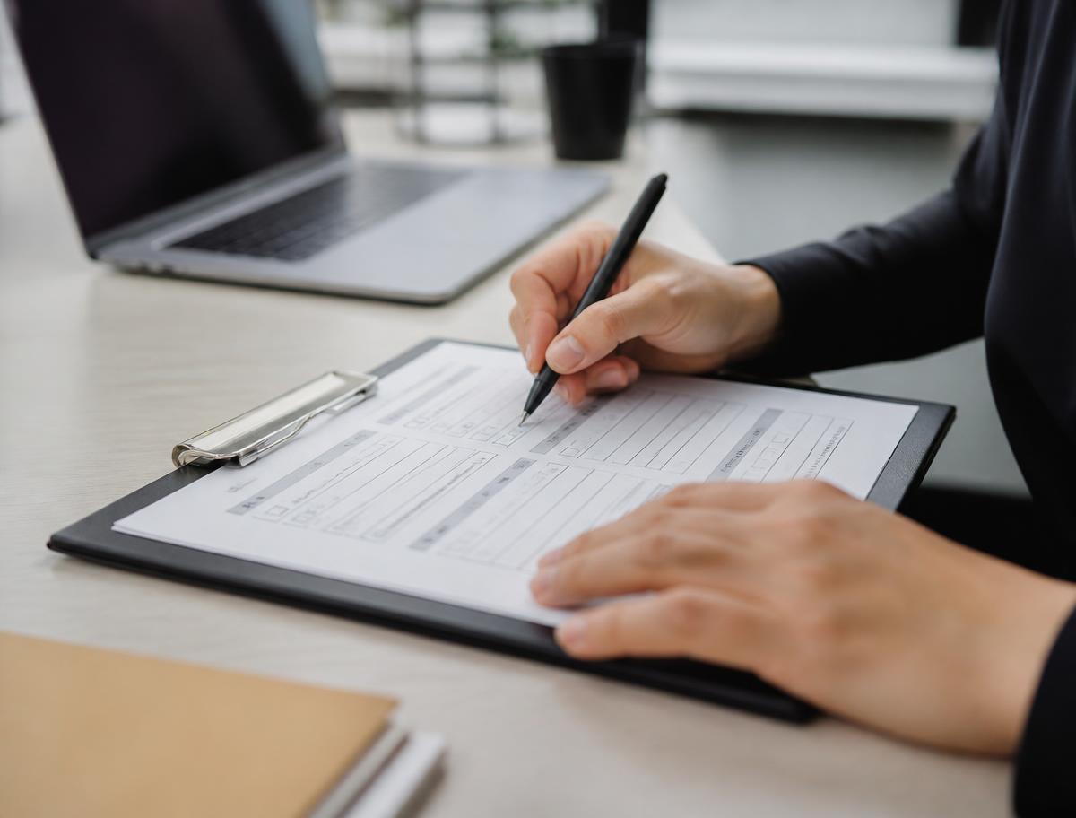 Hands filling in a short structured worksheet on a clipboard at a desk