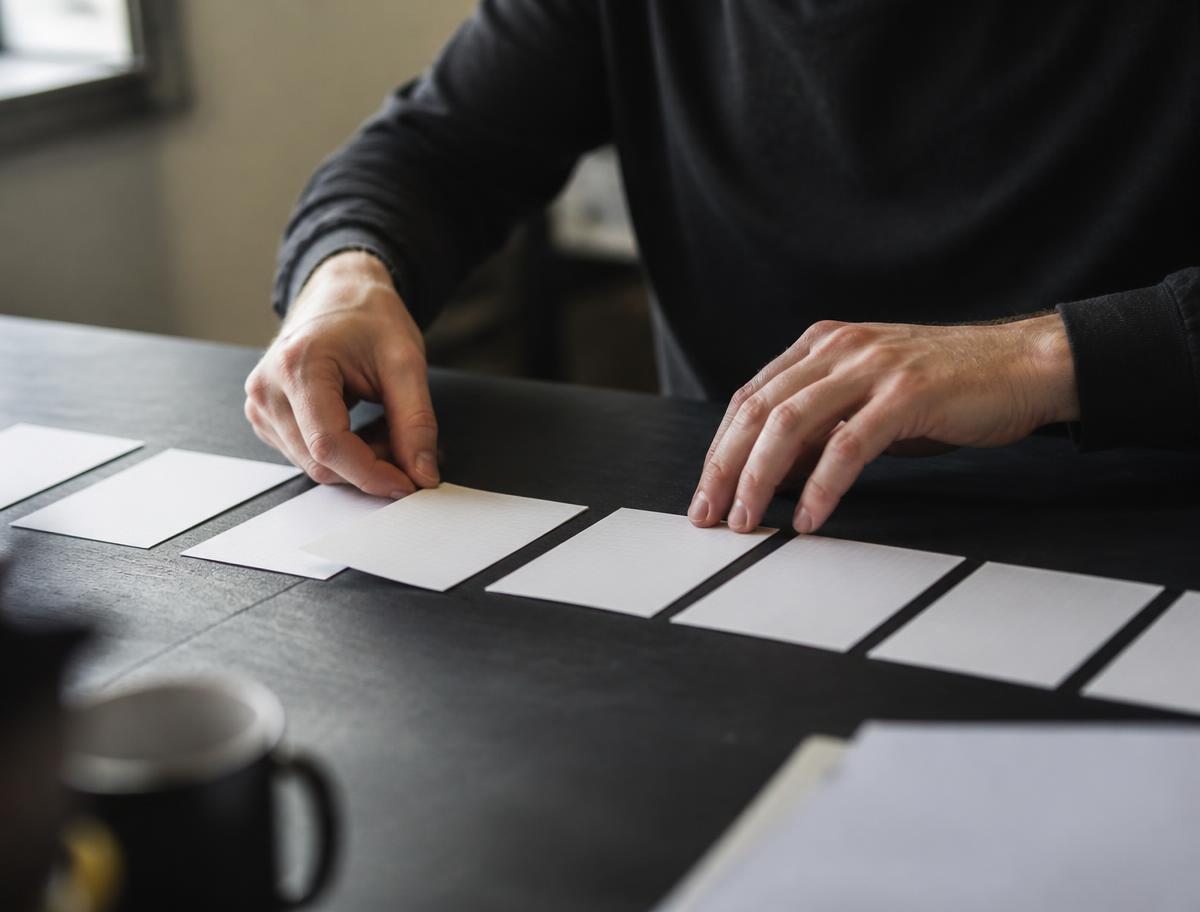 Hands laying index cards in a row across a desk, ordering them into a sequence