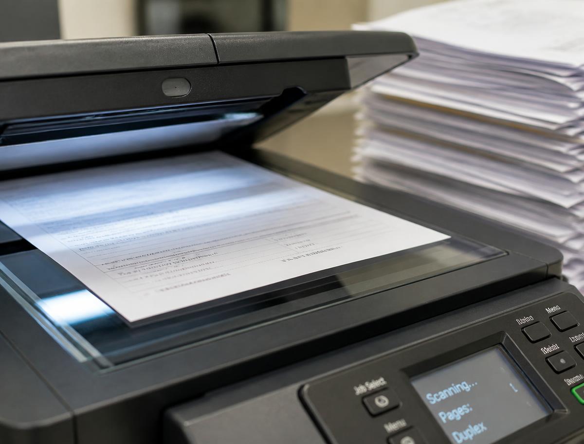 A close-up of an office scanner mid-scan with a stack of paper documents beside it