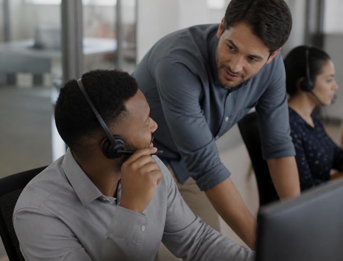 A support agent with a headset picking up a handed-over conversation while a colleague leans in