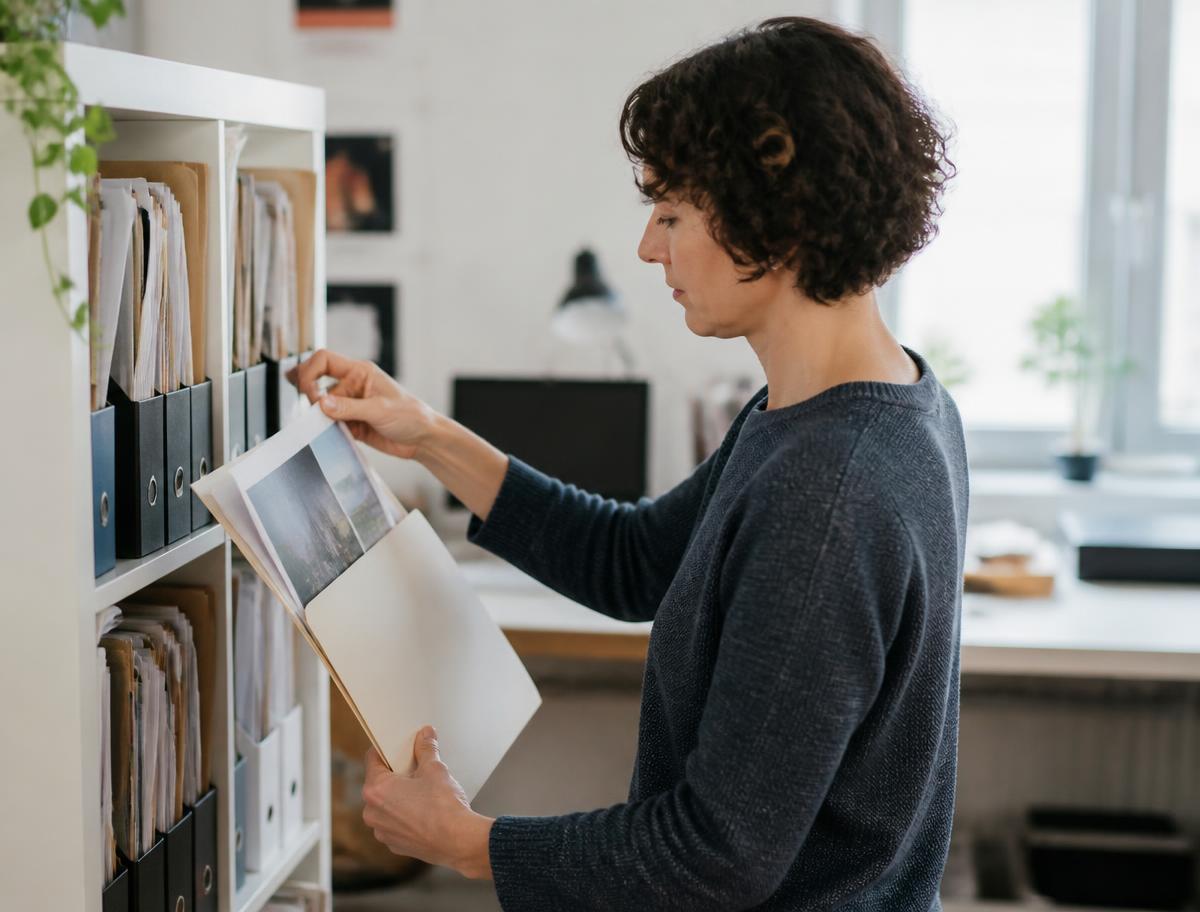 A person filing labelled printed versions into a folder on a shelf