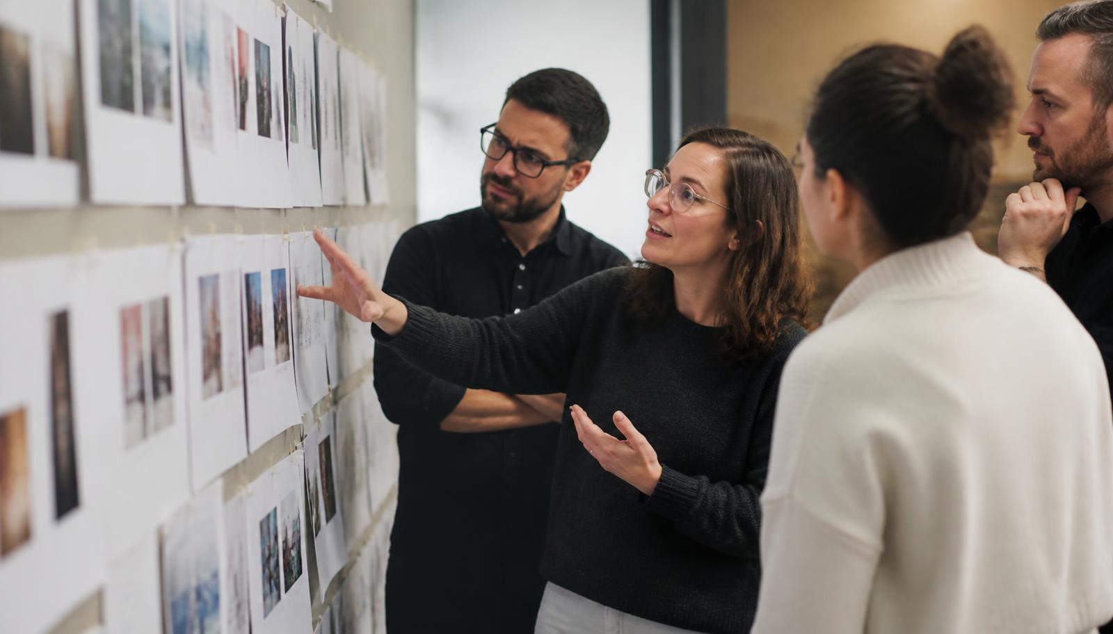 A marketing team at a wall of pinned printed campaign variants deciding which to keep